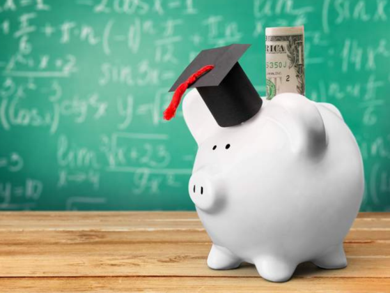 Piggy bank with graduation cap with dollar bill poking up its back. Background of a chalk board.